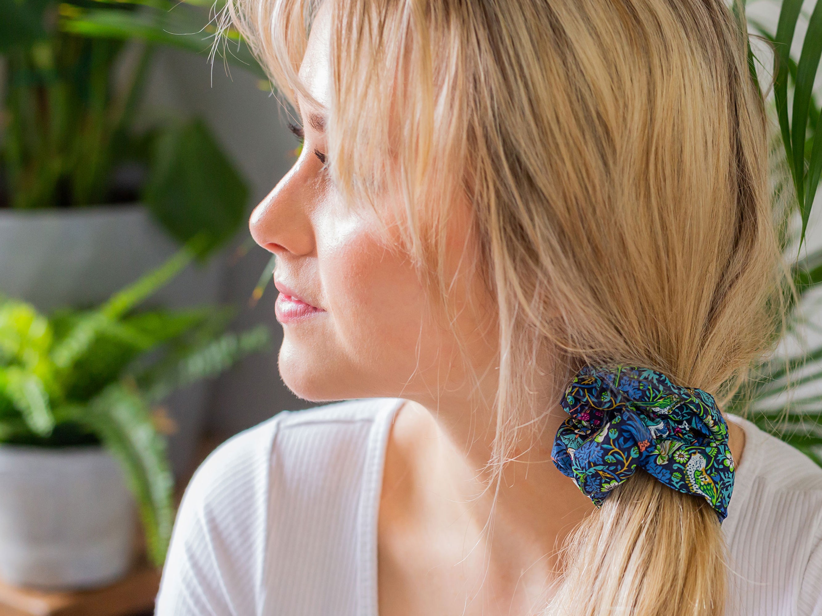 Woman with a blue scrunchie in her hair, surrounded by plants | Liberty London Print Scrunchie | Holme & Moss