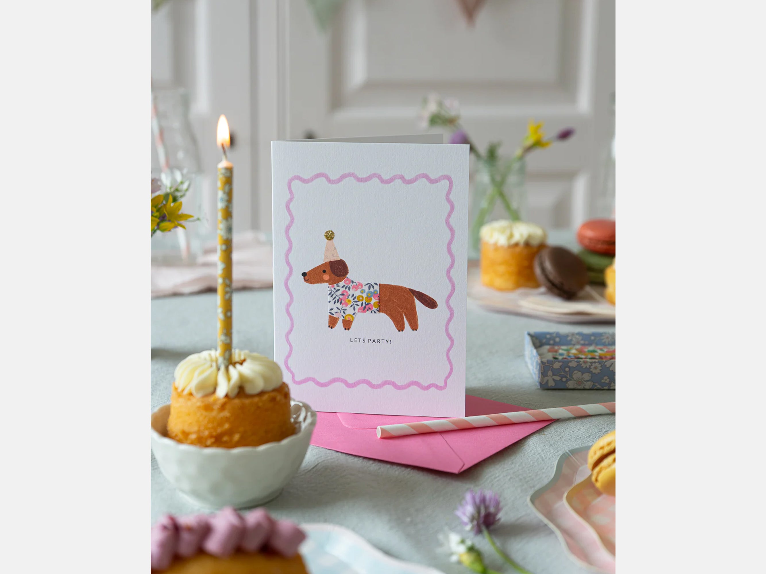 Greeting card with a dog illustration on a table with a cake and candles. | Sausage Dog Birthday Card - Liberty Wiltshire Bud Print | Holme & Moss