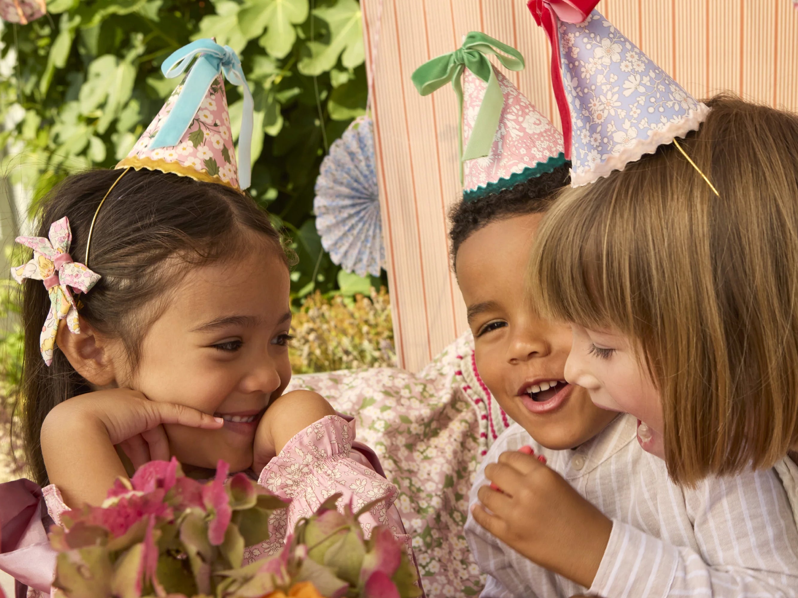 Three children wearing Liberty party hats, smiling and interacting with each other outdoors | Meri Meri x Liberty 8 Party Hats | Holme & Moss
