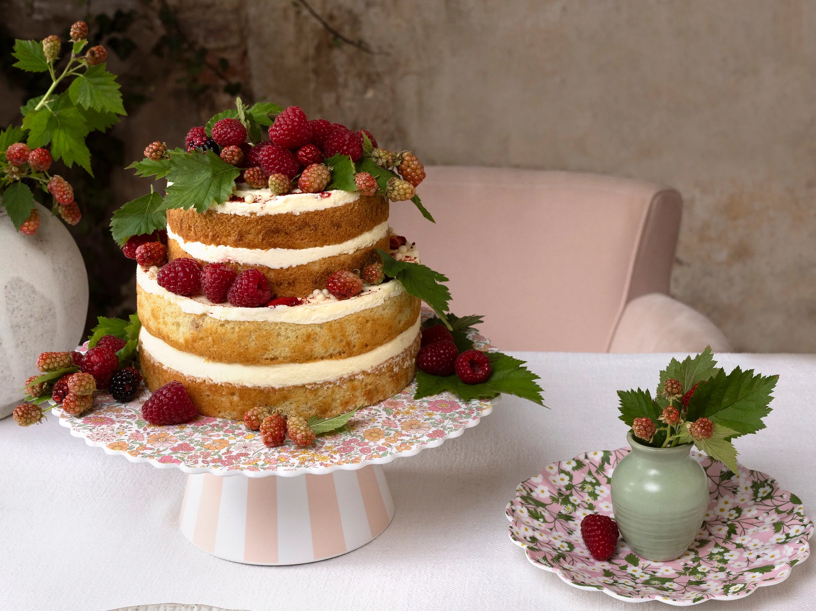 Three-tiered cake with berries on a floral cake stand, surrounded by decorative elements | Meri Meri x Liberty Reusable Cake Stand | Holme & Moss